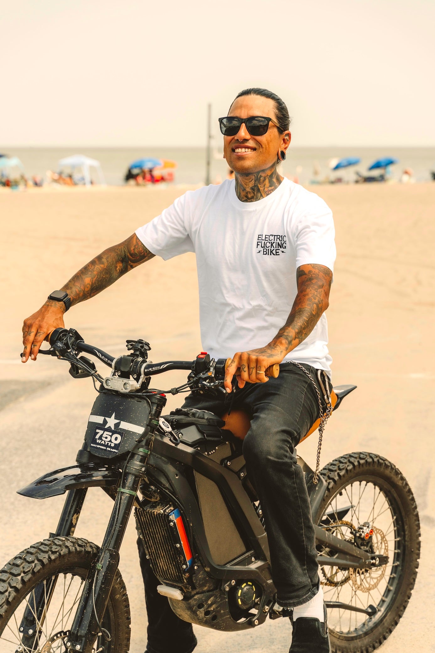 Man riding an electric bike on a beach with an Electric Bike shirt and sunglasses.