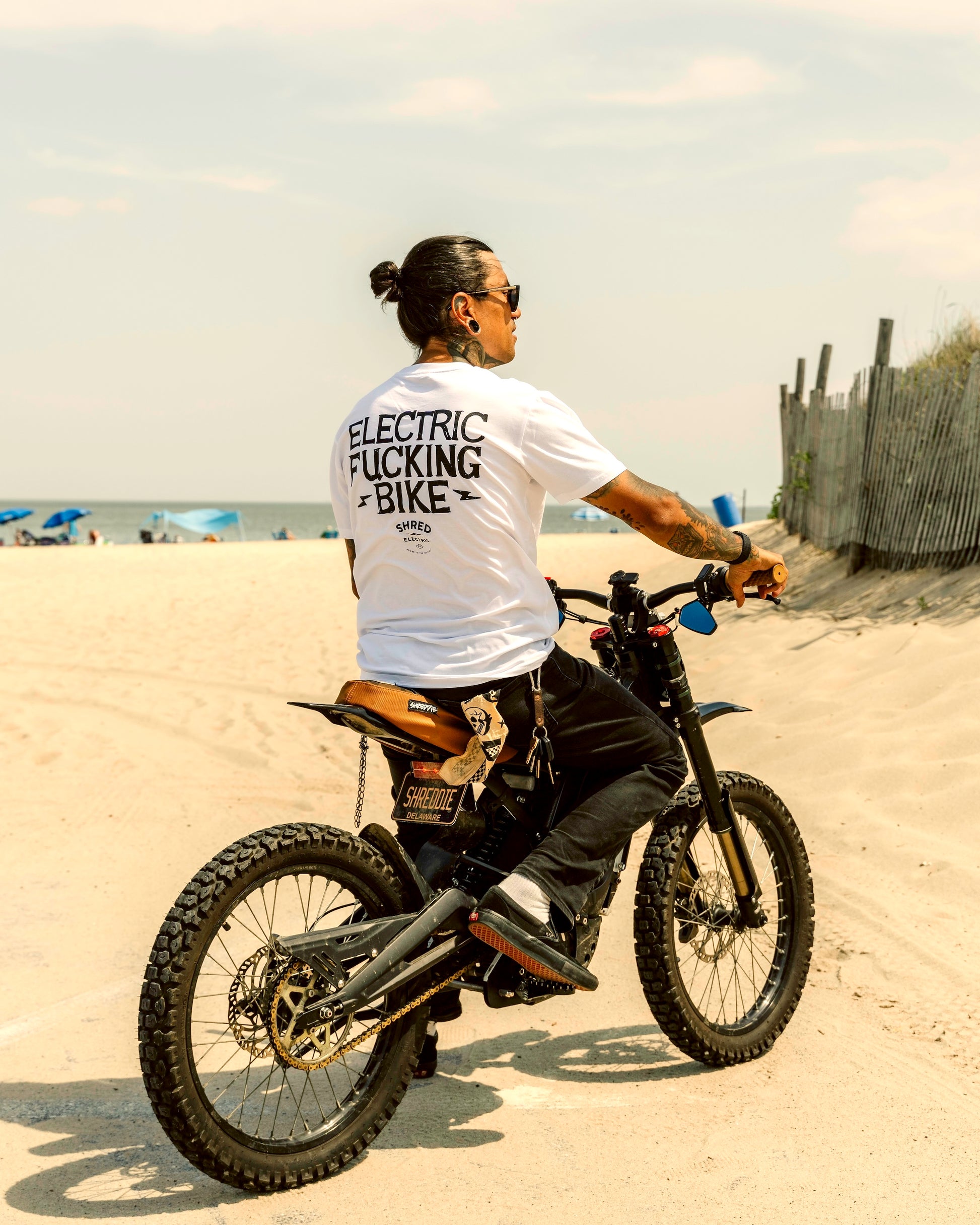 Person riding a bike on a sandy beach with "Electric Bike" text on their shirt.