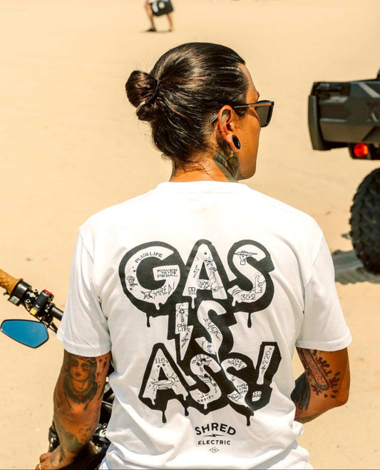 Gas Is Ass white t-shirt back with tattoo print text on the back, on a bike in a desert-like setting.