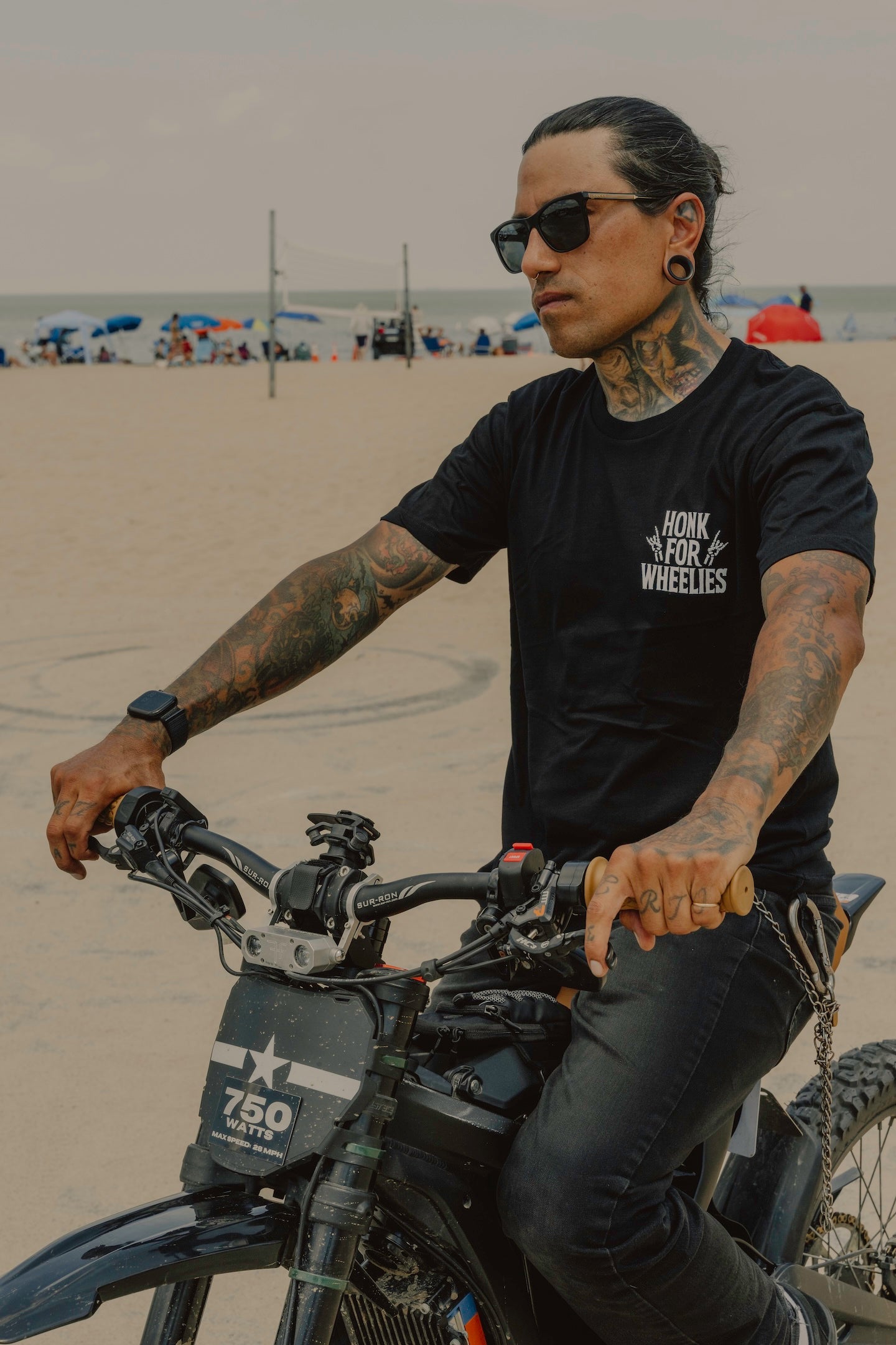 Honk For wheelies t-shirt on person riding a bike on a beach with a tattooed arms and sunglasses.