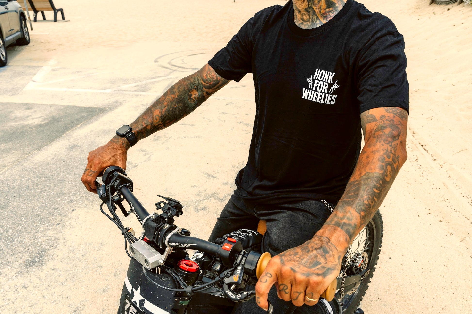 Person wearing a Honk for Wheelies black t-shirt with text, sitting on a motorcycle.