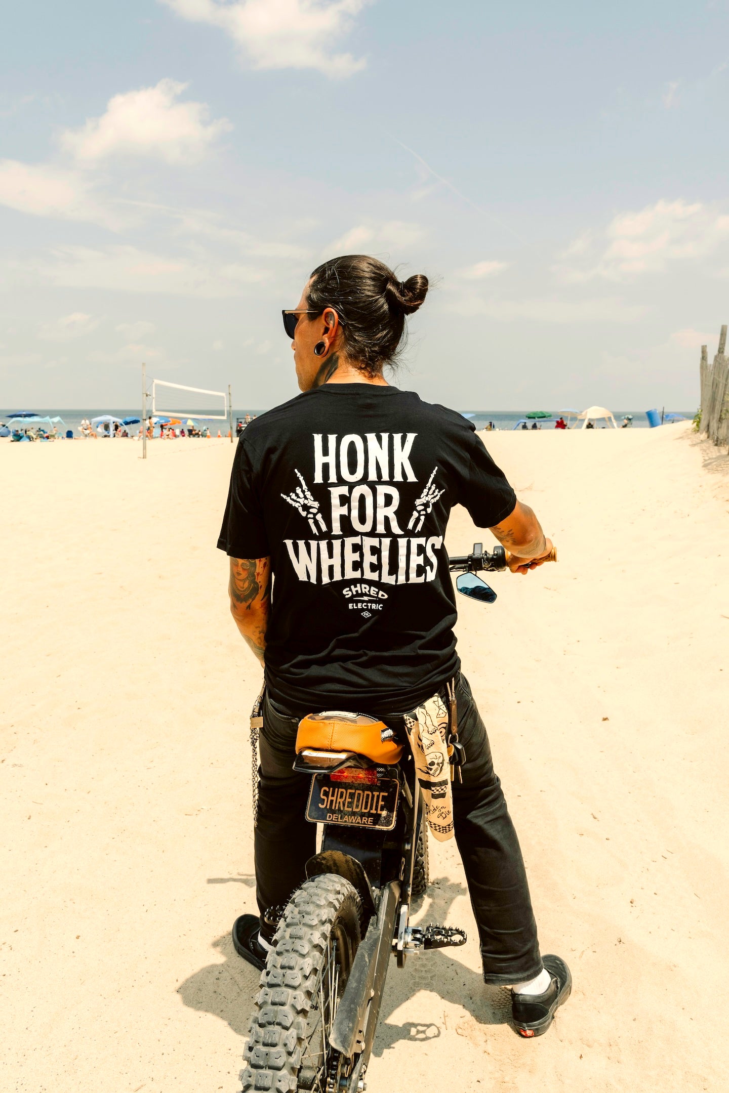 Honk For Wheelies shirt back view on person riding an electric dirt bike on the beach