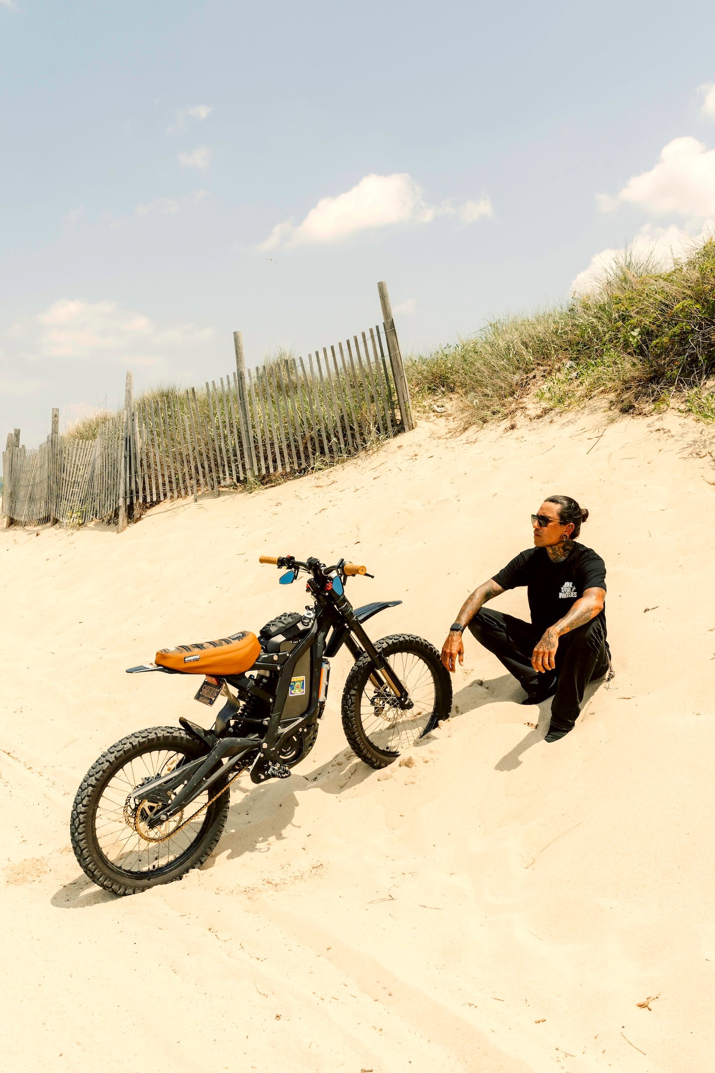 Honk for wheelies black t-shirt on person sitting next to a bike on a sandy beach