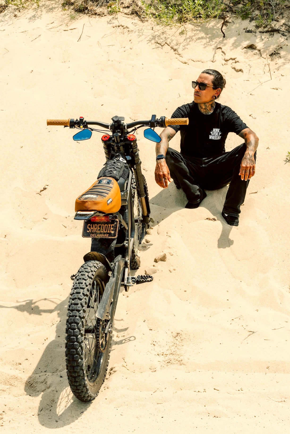 Honk For Wheelies shirt text on a person sitting on sand next to a dirt bike with 'Shreddie'"shred electric' branding