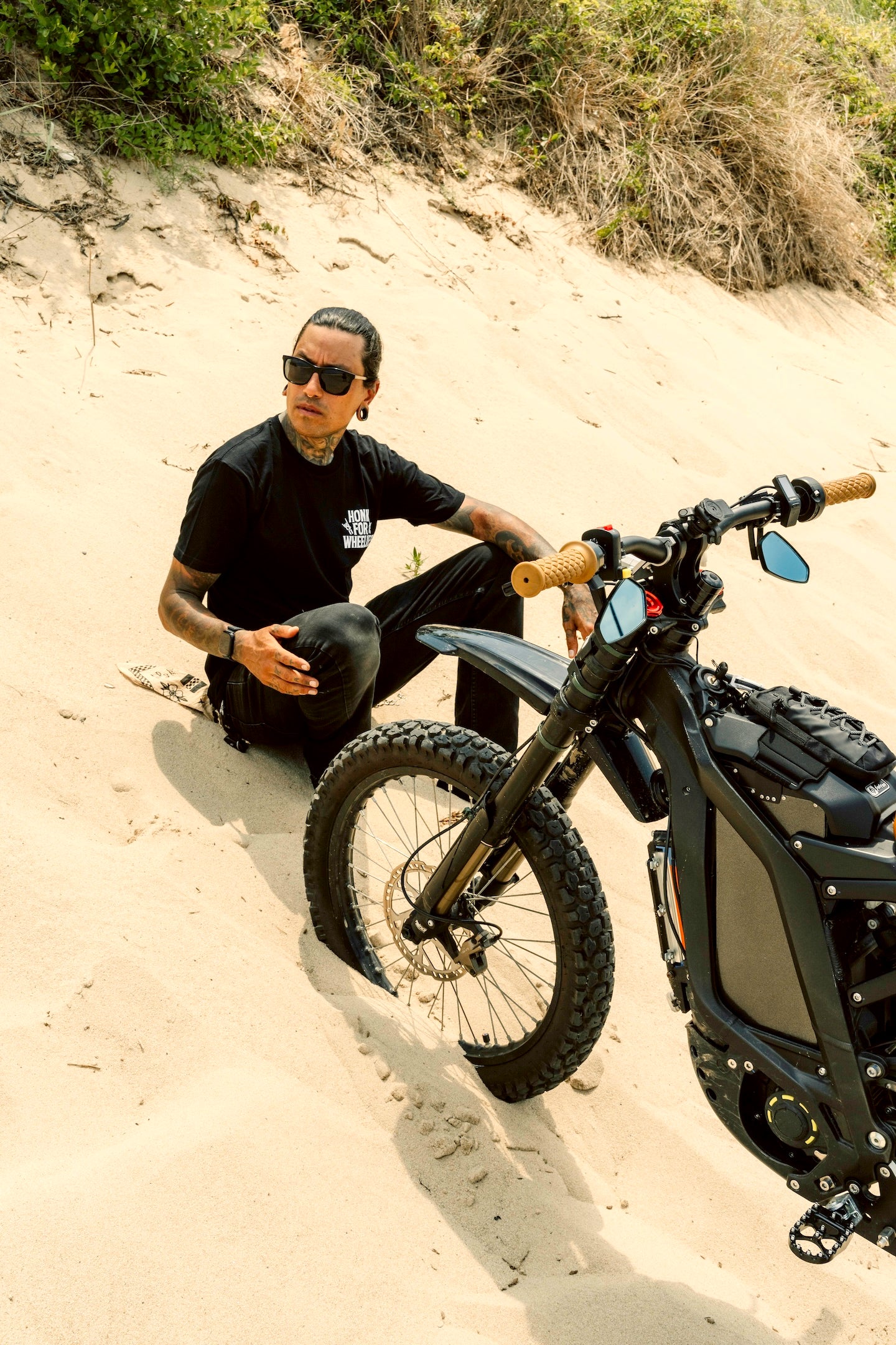 Honk For Wheelies shirt on person sitting on a sandy hill with a black motorcycle