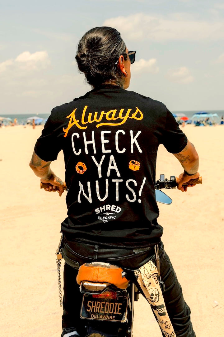 Person wearing a black t-shirt with a humorous Check Ya Nuts shirt on a bike.