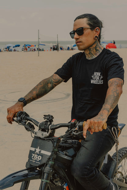 Honk For wheelies t-shirt on person riding a bike on a beach with a tattooed arms and sunglasses.