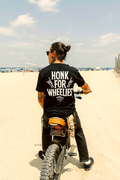 Honk For Wheelies shirt back view on person riding an electric dirt bike on the beach