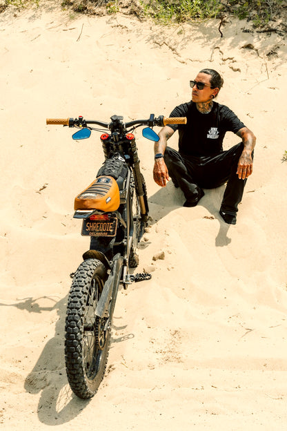 Honk For Wheelies shirt text on a person sitting on sand next to a dirt bike with 'Shreddie'"shred electric' branding
