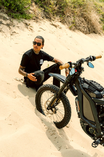 Honk For Wheelies shirt on person sitting on a sandy hill with a black motorcycle