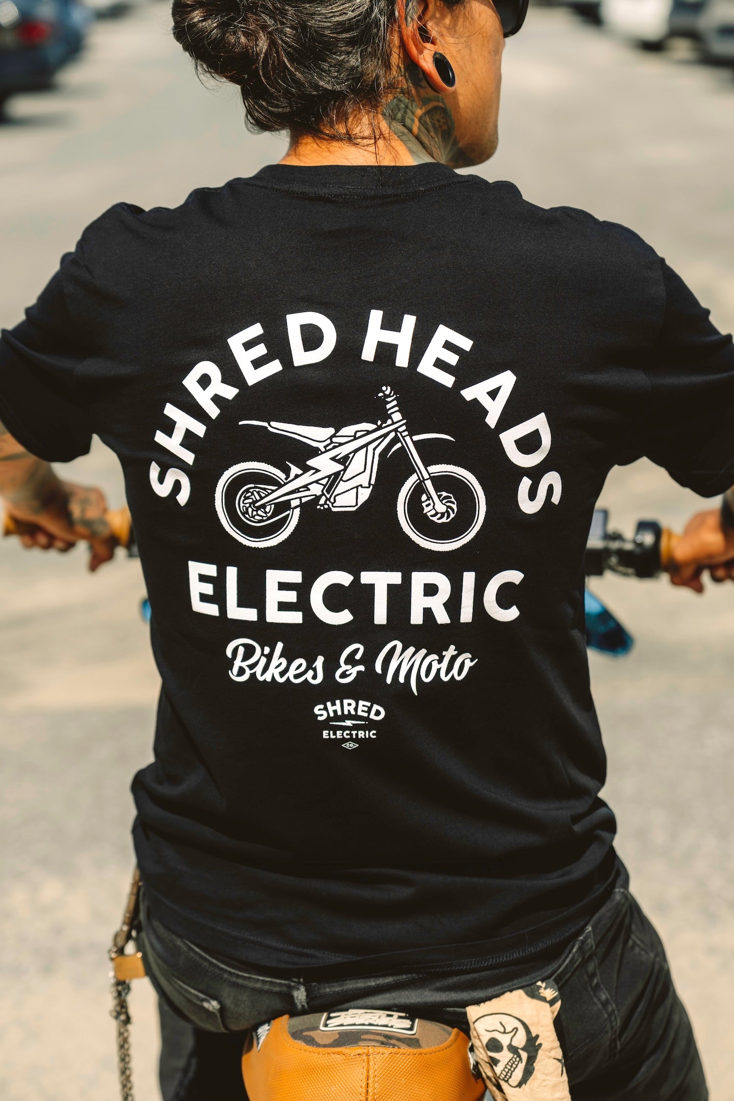Person wearing a black t-shirt with 'Shred Heads Electric bike & moto shirt' branding on a street background